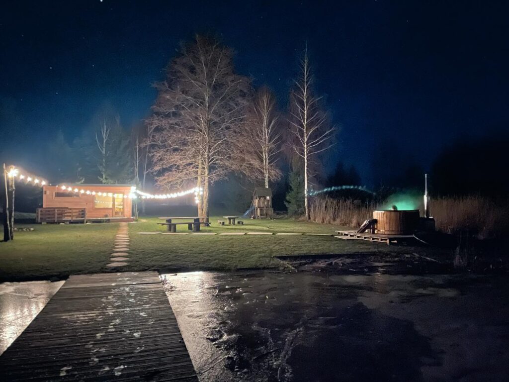 Drewniana sauna i balia nad zamarzniętym jeziorem w zimowej scenerii.